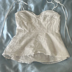 Vit linnetopp med knytband - Supersöt vit linnetopp med smala knytband och lätt utsvängd nederdel. Toppen har markerade kupor och smock i ryggen för extra komfort. Perfekt för varma dagar och fester💗