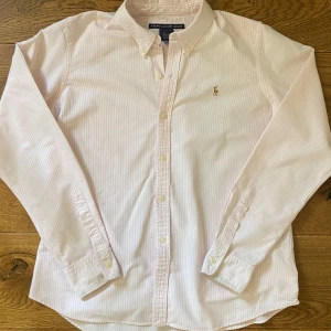 Randig Ralph Lauren skjorta - Mycket fint skick, utan defekter. Rosa och vitrandig. Storlek S, passar dig runt 170-180 cm. Kom gärna med prisförslag eller andra frågor!