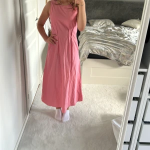 Rosa långklänning från Gestuz - Supersöt rosa långklänning från Gestuz i bomull. Klänningen är ärmlös med rund halsringning fram och snygg v-ringning i ryggen. Den har en rak, flowy passform och stängs med dragkedja bak. Perfekt för dig som vill ha en enkel men stilren look.