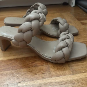 Beige flätade sandaler med klack H&M - Stilrena sandaler från H&M i beige med chunky flätade remmar och fyrkantig tå. Skorna har en låg klack och är tillverkade i syntetmaterial som ger en mjuk känsla. Perfekta för dig som vill ha en trendig och bekväm look.
