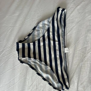 Randiga bikiniunderdelar i marinblått - Snygga bikiniunderdelar med breda marinblå och vita ränder. Klassisk midja och bekväm passform, perfekta för stranden eller poolen. Tillverkade i ett stretchigt syntetmaterial som torkar snabbt.