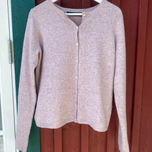 Ljusrosa kofta från Vero Moda - Lusrosa kofta från Vero Moda med rund halsringning och knappar framtill. Koftan är stickad och har långa ärmar.