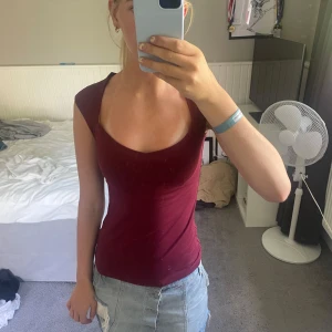 Vinröd tight topp med djup ringning - Säljer en vinröd, tight topp med djup rundad ringning och korta ärmar, köpt på bikbok 