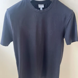 Svart t-shirt från Armani Collezioni - En stilren svart t-shirt från Armani Collezioni med diskret logga på bröstet. Klassisk rund halsringning och korta ärmar. Tillverkad i mjuk bomull som känns skön mot huden. Perfekt för dig som gillar minimalistisk och clean stil.