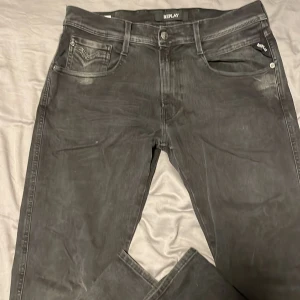 Replay Anbass svarta jeans - Snygga svarta Replay Anbass jeans med klassisk femficksdesign och diskreta slitningar. Jeansen har raka ben och normal passform, tillverkade i mjukt denimtyg med Replay-logga på fickan. Perfekta för en stilren och avslappnad look.