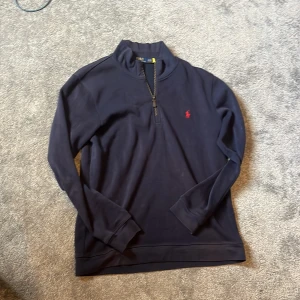 Marinblå half zip från Polo Ralph Lauren - Säljer en marinblå långärmad tröja från Polo Ralph Lauren med half zip och klassisk röd logga broderad på bröstet. Tröjan är i bomull och har en stilren, enkel design som funkar till allt. Perfekt för dig som gillar preppy och avslappnad stil.