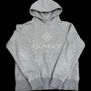 Grå Gant Hoodie - Mjuk och bekväm hoodie i ljusgrå färg med klassisk GANT-logga broderad framtill.  Storlek: 170 (passar ca 14–15 år).  Fint skick, utan skador eller fläckar.  Material: Bomullsblandning (mjuk insida).  Perfekt för vardagsbruk.