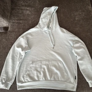 Ljusblå hoodie från YOURTURN - Snygg ljusblå hoodie från YOURTURN med klassisk känguruficka och dragsko i huvan. Tröjan är i mjuk bomullsblandning och har en stor relaxed passform med långa ärmar och ribbade muddar. Perfekt för chill dagar eller när du vill ha en clean look.