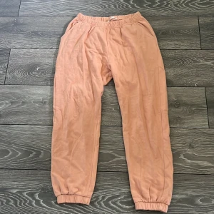 Ljusrosa mjukisbyxor med resår - Säljer ett par ljusrosa mjukisbyxor med resår i midjan och vid bensluten. Byxorna har en avslappnad passform och är tillverkade i mjukt bomullstyg, perfekta för chill dagar. Fickor på sidorna för extra bekvämlighet.