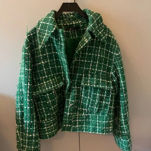 Grön jacka från Gina tricot  - Trendig grön jacka från Gina med rutigt mönster i vitt. Jackan har stora fickor framtill, klassisk krage och knappar som tyvärr inte används längre 