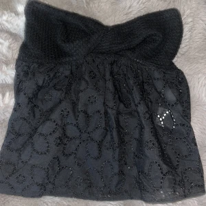 Svart bandeau tubtopp med blommönster - Supersöt svart bandeau tubtopp med stickad, twistad överdel och broderade blommor på tyget. Toppen är ärmlös och har en luftig passform nedtill. Perfekt för dig som vill ha en unik och trendig look med coola detaljer.