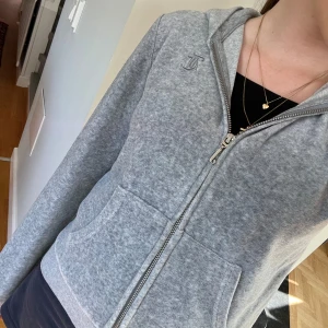Grå hoodie från Juicy Couture - Mysig grå hoodie från Juicy Couture med dragkedja framtill och broderad logga på bröstet. Tröjan har huva, fickor och ribbade muddar vid ärmslut och nederkant. Nästan helt oanvänd.