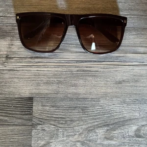 Raybans boyfriend liknande - Snygga solglasögon med bruna, fyrkantiga bågar och tonade glas. Klassisk modell som ger en cool vibe och passar perfekt till sommaren. Bågarna är i plast och har en stilren look. Helt nya