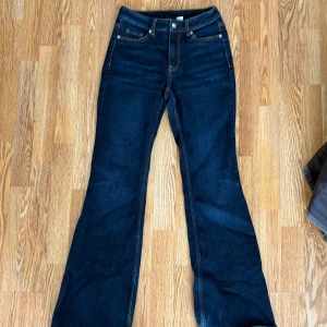 Mörkblå bootcut jeans i storlek 34 - Snygga mörkblå jeans med bootcut-modell och klassiska kontrastsömmar. Byxorna har fem fickor och normal midja, perfekta för dig som gillar en tidlös och cool look. Materialet är klassisk denim som sitter skönt hela dagen.