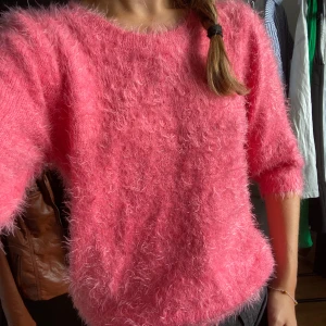 Fluffig rosa stickad tröja - Supermjuk och fluffig rosa stickad tröja med trekvartsärm. Tröjan har en rund halsringning och är perfekt för dig som vill ha en mysig och trendig look. Passar lika bra till jeans som till kjol för en chill vibe.