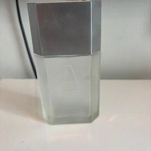 Azzaro Pour Homme parfymflaska (tom flaska) - Stilren parfymflaska från Azzaro med frostat glas och en stor, silverfärgad, sexkantig metallkork. Flaskan har en modern och maskulin design med Azzaro-loggan ingraverad på locket. Perfekt för dig som gillar klassiska och eleganta dofter.