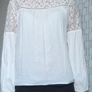 Vit blus med spetsdetaljer - Säljer en vit blus med långa ärmar och vackra spetsdetaljer över axlar och upptill. Blusen har en lös passform och är perfekt för dig som gillar romantiska och feminina plagg. Superfin att styla med både jeans och kjol.
