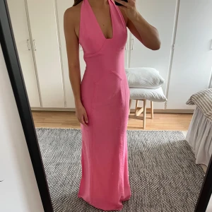 Oanvänd rosa långklänning från Adoore - Supersnygg långklänning i hot pink från Adoore. Klänningen har halterneck som man knyter i nacken, djup v-ringning och slits på sidan. Dessutom är hela klänningen fodrad och har en gömd dragkedja. Man får en sååå fin silhuett och som referens är jag 165 cm 💕Nypris: 1595kr Klänningen har aldrig använts!!