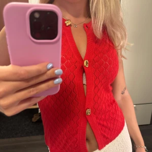 Röd stickad väst med guldknappar XS - Snygg röd stickad väst från gina tricot i storlek XS. Västen har ett diskret diamantmönster, v-ringning och coola guldiga knappar framtill. Perfekt att styla över en t-shirt eller linne för en trendig look. Materialet är mjukt och andas, vilket gör den skön att bära.