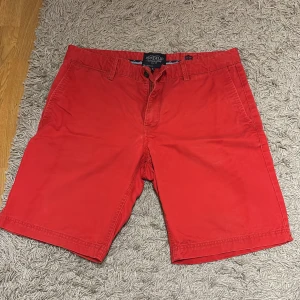 Röda shorts från Bondelid - Snygga röda shorts från Bondelid med klassisk passform och bälteshällor. De har två fickor fram och två bakfickor, perfekta för sommardagar. Tillverkade i mjuk bomull som känns skön mot huden. Enkla att matcha med t-shirt eller skjorta för en chill look.
