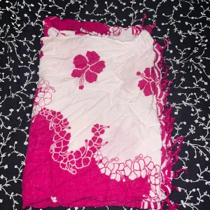 Vit och rosa blommig halsduk - Snygg halsduk i vitt och rosa med stora blommor och fransar längs kanterna. Perfekt accessoar för att liva upp din outfit med ett färgglatt och lekfullt mönster. Tunn och mjuk, passar bra till vår och sommar.