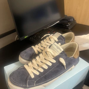 2025 Philippe Model blåa skor kvitto finns? - Snygga sneakers från Philippe Model i blå mocka med beige detaljer och vita skosnören. Skorna har rund tå, platt sula och kontrasterande hälparti i beige skinn. Perfekta för dig som gillar stilrena och exklusiva sneakers med lyxig känsla.