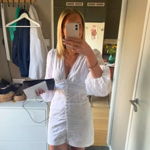 Adoore klänning - Supersöt vit kort klänning med v-ringning och puffiga långärmar. Klänningen har knappar framtill och markerad midja som ger en snygg form. Perfekt för sommaren💞💞