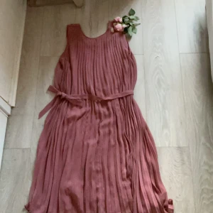 Plisserad rosa klänning med knytband (köpt för 1900) - Superfin plisserad klänning i dammigt rosa med knytband i midjan och broderade detaljer vid axlarna. Ärmlös modell med rund halsringning och mjukt, flowy tyg som ger en snygg siluett. Perfekt för sommarens alla tillfällen!