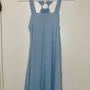 Ljusblå ärmlös klänning med ringdetalj - Supersöt ljusblå klänning med breda axelband och unik ringdetalj i ryggen. Klänningen är ärmlös och har en luftig, rak passform som faller snyggt. Perfekt för varma dagar när du vill känna dig både chill och stylish.