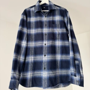 Blårutig skjorta från Uniqlo - Snygg blårutig skjorta från Uniqlo i 100% bomull. Skjortan har klassisk krage, knäppning framtill och en bröstficka. Mönstret är i olika nyanser av blått och vitt, perfekt för en avslappnad och stilren look.