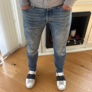 Jack & Jones Slitna Jeans  - !! NYSKICK !!Säljer ett par Jack & Jones jeans i Slimfit storlek 31/32  i klassisk blå tvätt med slitningar och snygga detaljer på knäna. Jeansen har fem fickor, normal midja och smal passform som sitter tajt hela vägen ner. Perfekta för dig som gillar en modern och avslappnad look.