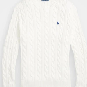 Vit kabelstickad tröja Polo Ralph Lauren - Vit kabelstickad tröja från Polo Ralph Lauren med klassisk blå logga broderad på bröstet. Tröjan har rund hals, ribbade muddar och lång ärm. Perfekt för lager-på-lager och snygg till både jeans och chinos.