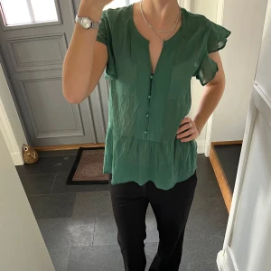 Grön kortärmad volangblus - Grön  kortärmad topp med knappar och volanger från Bodyflirt i storlek 38. Fint skick. Använd gärna köp nu!