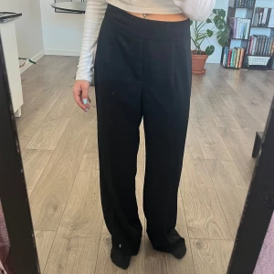 Kostymbyxor - Högmidjade kostymbyxor med dragkedja på sidan.