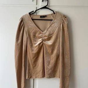 Beige sammetsblus från KappAhl XS - Supersnygg beige sammetsblus från KappAhl i storlek XS. Blusen har lång ärm, v-ringning och snygg rynkdetalj framtill. Materialet är mjukt och glansigt, vilket ger en lyxig känsla. Perfekt för dig som vill sticka ut lite extra.