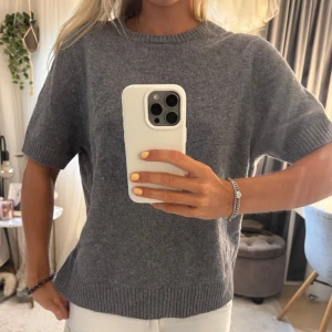 Grå stickad kortärmad tröja från Zara - Mysig grå stickad tröja från Zara med korta ärmar och rund hals. Tröjan har ribbade muddar vid ärmslut och nederkant, vilket ger en clean och stilren look. Perfekt att matcha med jeans eller kjol för en chill vibe. Passar mig som vanligtvis har s-m