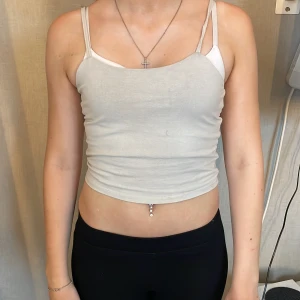 Ljusgrå croppad linnetopp XOXO friends - Säljer en ljusgrå croppad linnetopp från XOXO friends. Toppen har smala axelband och är figurnära med enkel, stilren design. Perfekt att matcha med höga jeans eller shorts för en chill look.