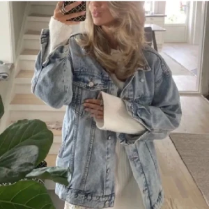 Oversized ljusblå jeansjacka - Säljer en oversized ljusblå jeansjacka med klassiska knappar framtill och två bröstfickor med lock. Jackan har en avslappnad passform och långa ärmar, perfekt att slänga över en hoodie eller t-shirt för en chill look. Använd en gång.