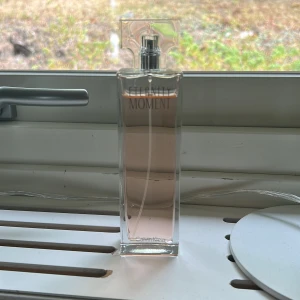 Eternity Moment parfym Calvin Klein - Eternity Moment från Calvin Klein i en elegant, rektangulär glasflaska med ljusrosa doftvätska. Flaskan har en stilren, transparent design och ett unikt, fyrkantigt lock. Perfekt för dig som gillar fräscha och blommiga dofter.