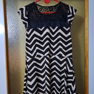 Svartvit klänning med spets och zigzag - Snygg kortklänning med svart och vit zigzag-mönster och mörkblå spets upptill. Klänningen har rund halsringning, korta ärmar och ett flowy fall. Dock så står det inte på den vart den kommer ifrån eller storlek- så det är en gissning :)
