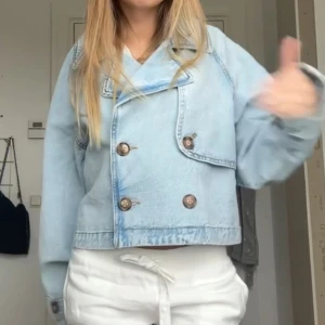 Ljusblå croppad jeansjacka med knappar - Säljer en ljusblå croppad jeansjacka med dubbelknäppning och stora bruna knappar. Jackan har oversized passform, bred krage och långa ärmar. Perfekt för dig som gillar en chill och trendig look. Materialet är klassisk denim och jackan är enkel att styla till olika outfits. Säljer denna eftersom den inte kommer till användning längre😊😊