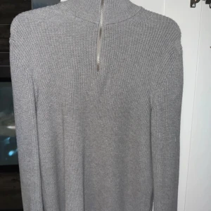 Grå stickad polotröja från Zara - Säljer en grå stickad polotröja från Zara i storlek M. Tröjan har en hög krage och en snygg half zip-dragkedja framtill. Perfekt för lager-på-lager och chill höst- eller vinterstil. Enkel att matcha med jeans eller kjol för en clean look.