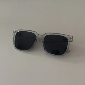 Transparenta fyrkantiga solglasögon - Snygga solglasögon med transparent båge och mörka fyrkantiga glas. Riktigt clean och modern look som passar perfekt till sommaren. Bågarna är i plast och har en stilren design som sticker ut utan att bli för mycket.
