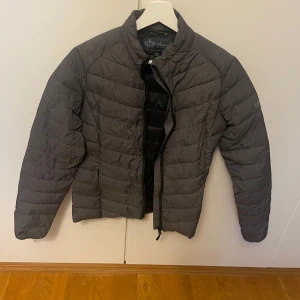 Grå dunjacka från Active Riding Wear S - Säljer en grå dunjacka från Active Riding Wear i storlek S. Jackan är quiltad med horisontella sömmar, har dragkedja framtill och diskreta fickor med dragkedja. Perfekt för kyliga dagar och har en clean, sportig look.