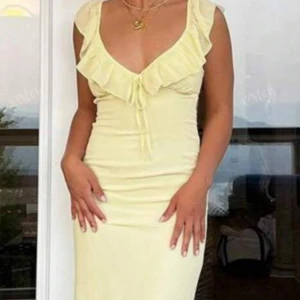 Alldrig använd!!Ljusgul långklänning med volang - Supersöt långklänning i ljusgul nyans med volangdetaljer vid urringningen och knyt framtill. Klänningen har smala axelband, öppen rygg med knyt och figurnära passform. Perfekt för sommarens alla tillfällen!