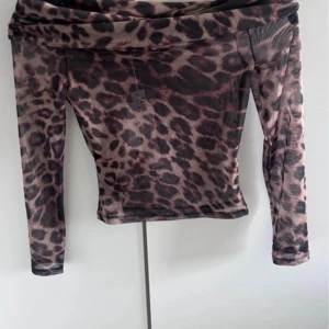 Leopardmönstrad mesh offshoulder topp - Snygg offshoulder topp från NA-KD i transparent mesh med leopardmönster i bruna och svarta toner. Långärmad och figurnära passform, perfekt för dig som vill sticka ut. Tunn och luftig känsla, passar till många olika looks.