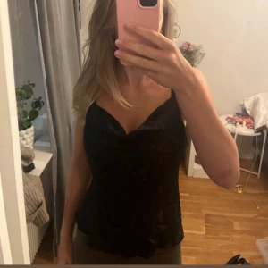 Svart satin topp  - Svart kort slipklänning från Kappahl med tunna justerbara axelband och snygg draperad urringning. Klänningen har en slät, lätt glansig yta och sitter figurnära. Perfekt för dig som gillar minimalistisk och stilren look.