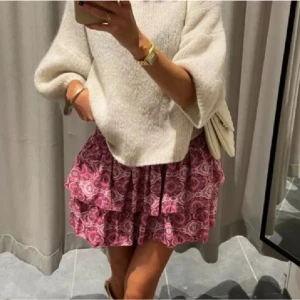 Rosa volangkjol från Meet x Tiger - Supersöt kort volangkjol från Meet x Tiger i rosa med paisleyinspirerat mönster. Kjolen har smock i midjan för en bekväm passform och dubbla volanger som ger en flowy och lekfull look. Perfekt att styla med stickad tröja eller crop top.