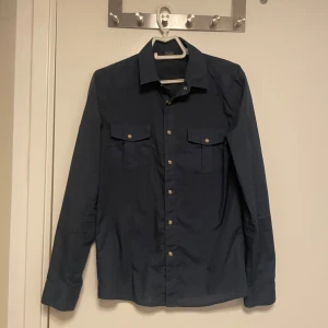 Mörkblå skjorta från Cheap Monday - Snygg mörkblå skjorta från Cheap Monday i klassisk modell med två bröstfickor och knappar framtill. Skjortan har lång ärm och stilren krage, perfekt för en clean och enkel look.