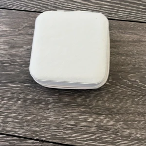 Vit smyckeskrin  - Snygg och praktisk liten smyckesplånbok i vitt med dragkedja runtom. Insidan har flera fack och rullar för ringar samt krokar för halsband eller örhängen. Perfekt att ha med sig i väskan eller på resan.